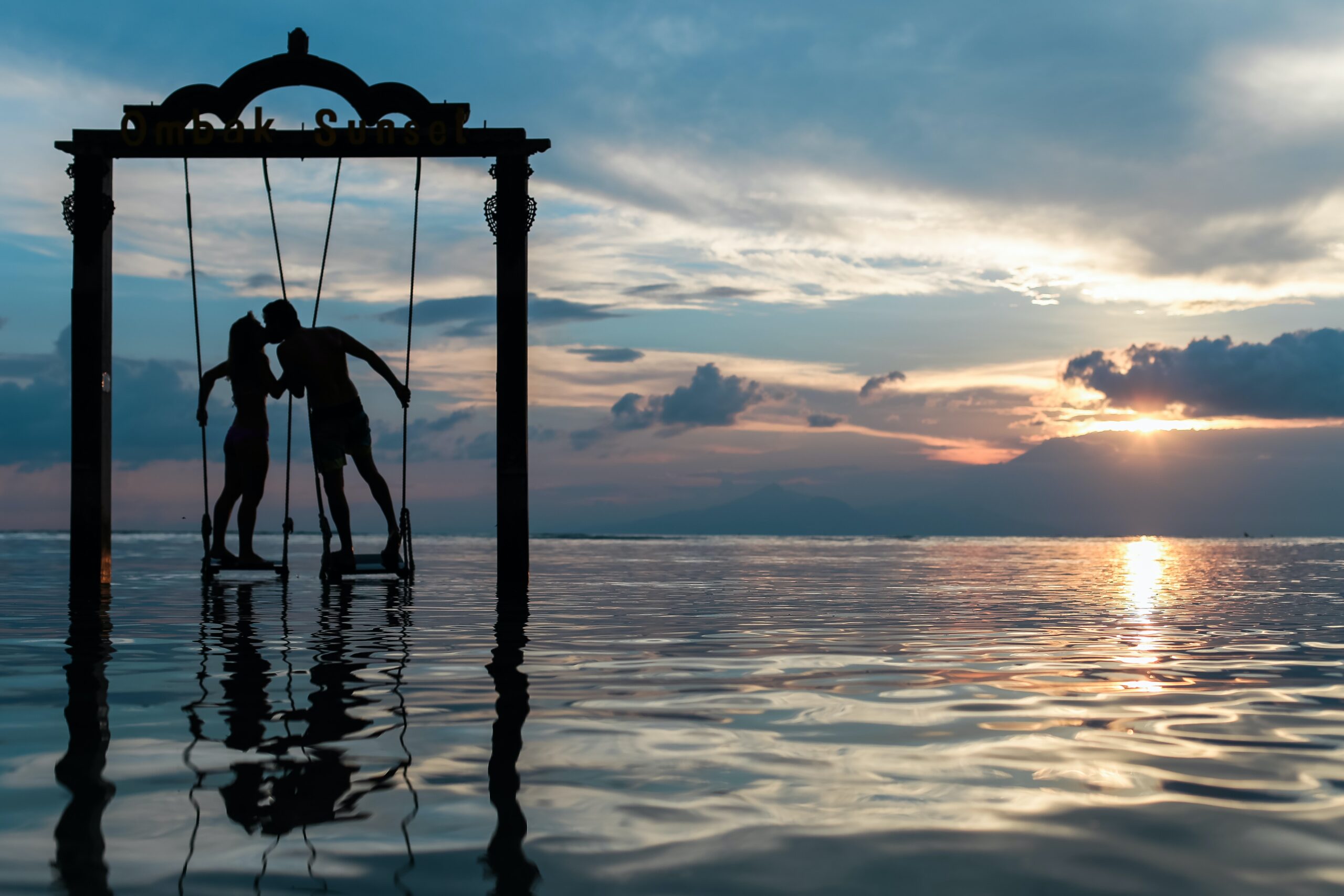 Couple embracing on swings over the water.